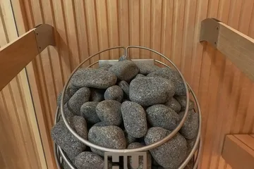 Auroom Libera Glass, at the heater: The HUUM heater's stones up close, the benches to the right, the showroom through the glass.