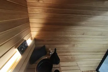 Auroom Mira L, lying back: Lying on the upper bench: the bucket and ladle nearby, the ceiling above.