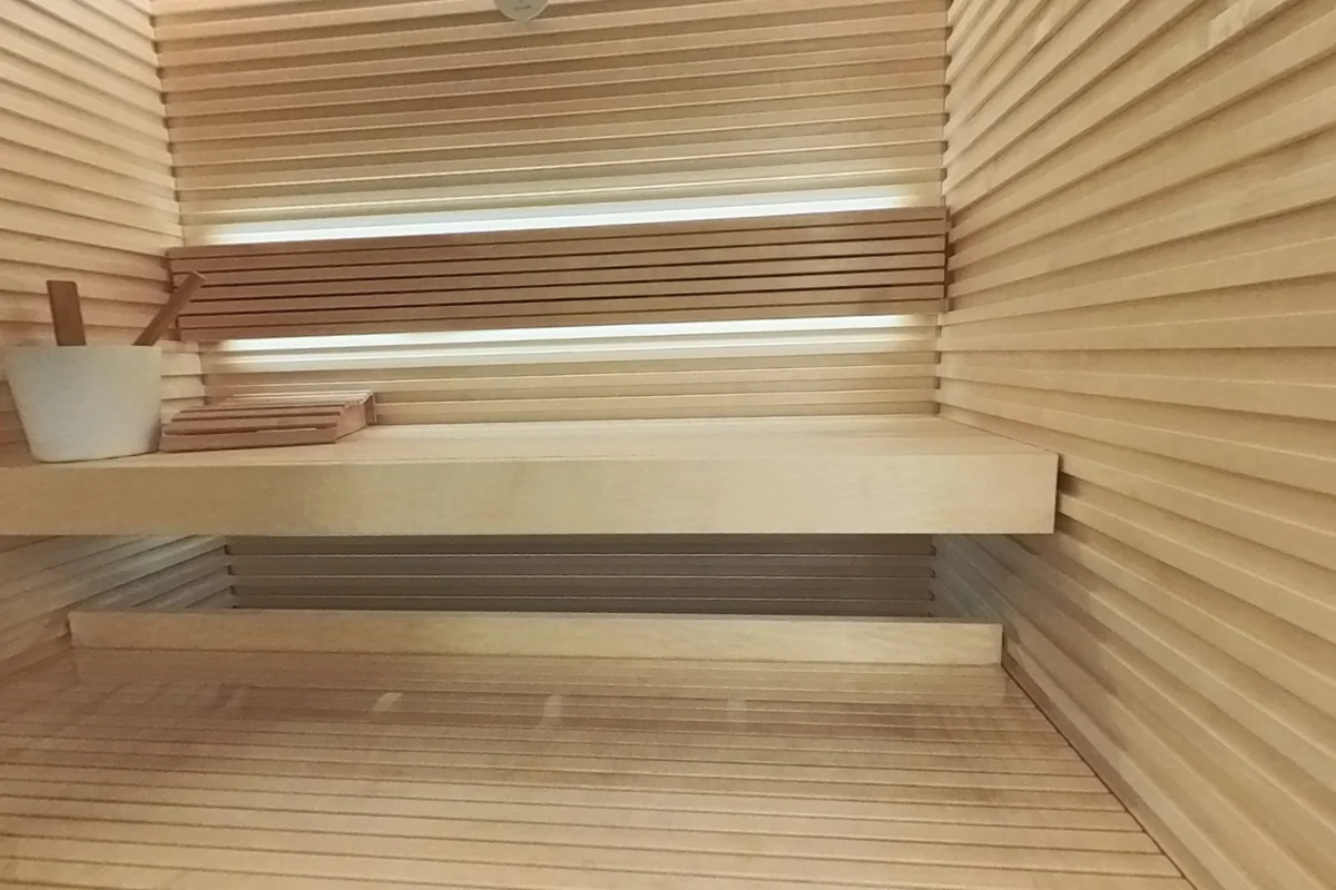Auroom Nativa Glass, inside the sauna: The two bench levels, profiled wood walls and heater beside the door.